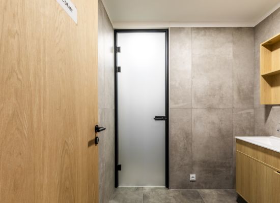 Kliknutím zvětšíte Stylové neprůhledné celoskleněné dveře SAPELI v černém kovovém rámu elegantně oddělují umývárnu, WC a další zázemí pro zaměstnance.