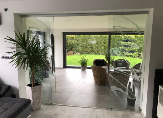 Kliknutím zvětšíte Skleněná stěna z kaleného bezpečnostního čirého skla s motivem, posuvný systém DORMA MUTO v nerezu, zakázková výroba spol. PRO-K