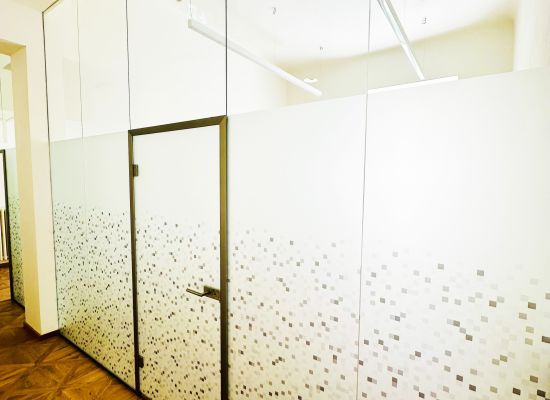 Kliknutím zvětšíte Detail celoskleněných dveří v rámu vsazených do skleněné stěny, která slouží jako příčka služebny policie. Soukromí zajišťuje potištěna fólie s elegantními designovými prvky.